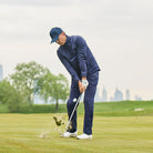 Man in navy golf outfit holding a golf club on a golf course