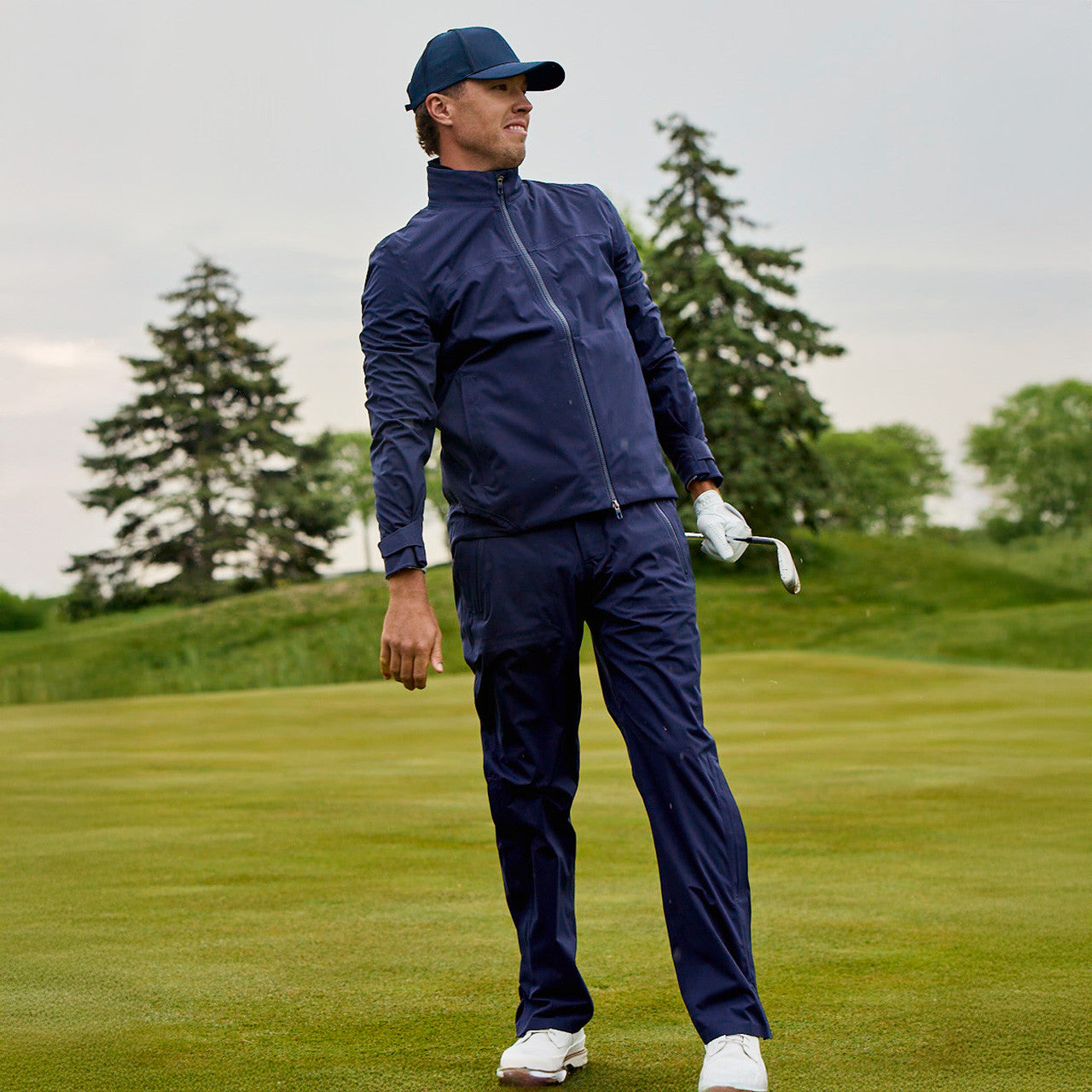 Man in navy golf outfit holding a golf club on a golf course