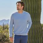 Man wearing a light blue sweater and pants standing in front of a cactus